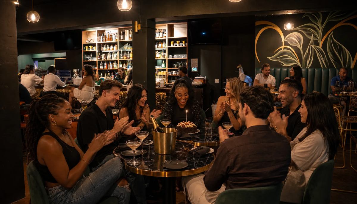 Birthday group of eight clapping around joined tables with champagne, martinis and a candlelit dessert at Spanglish Martini Bar in Wynwood, Miami