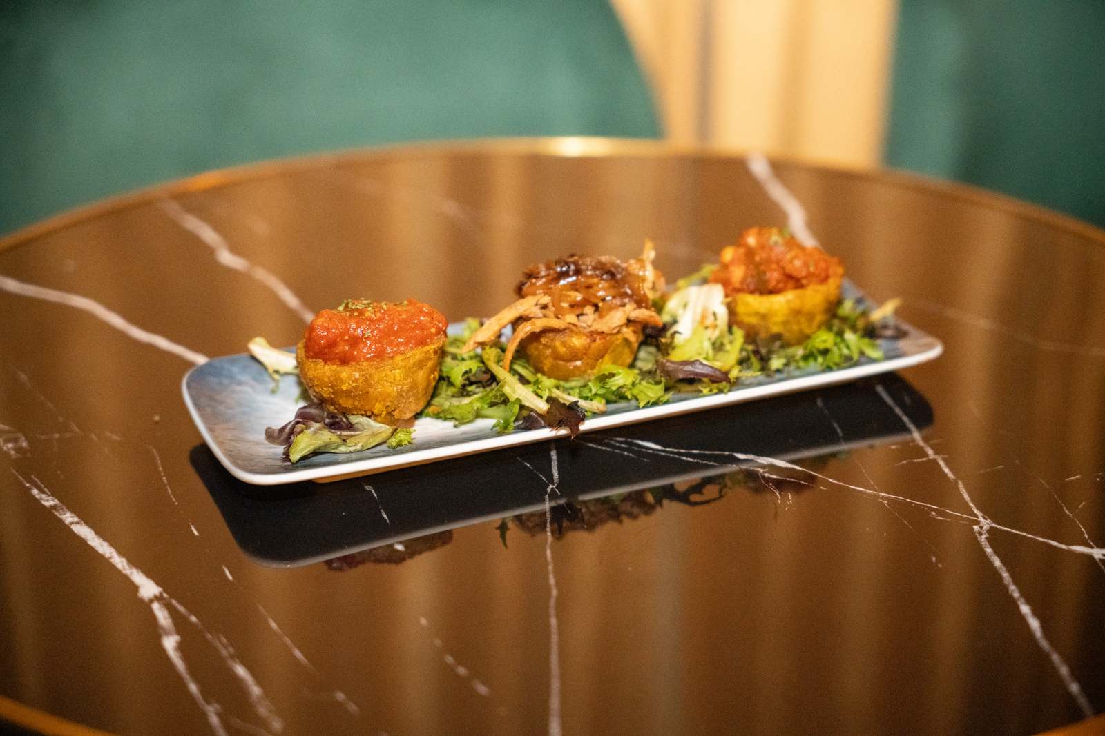 Trio of fried pastry cups with meat, bean and sauce toppings on a narrow plate on a dark tabletop at Spanglish Martini Bar in Wynwood, Miami