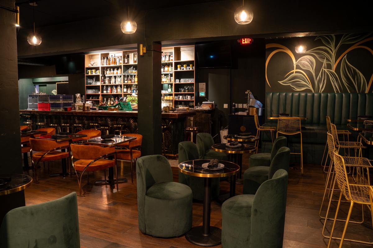 Green velvet swivel chairs and brass-trimmed tables in front of the lit back bar at Spanglish Martini Bar in Wynwood, Miami