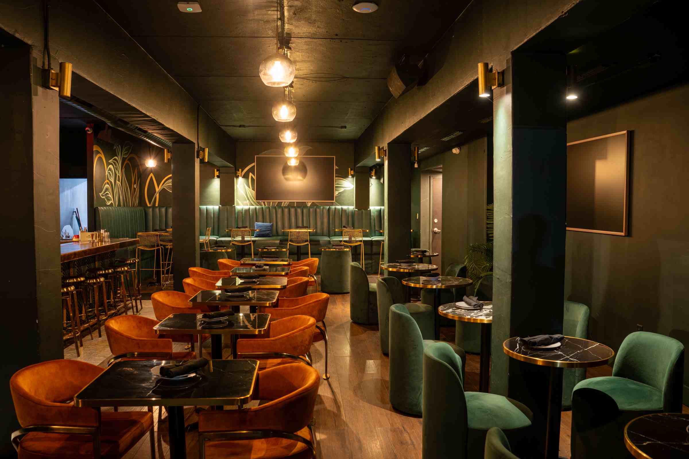 The lounge at Spanglish Martini Bar in Wynwood, Miami: rows of round tables with green and rust velvet chairs under pendant light