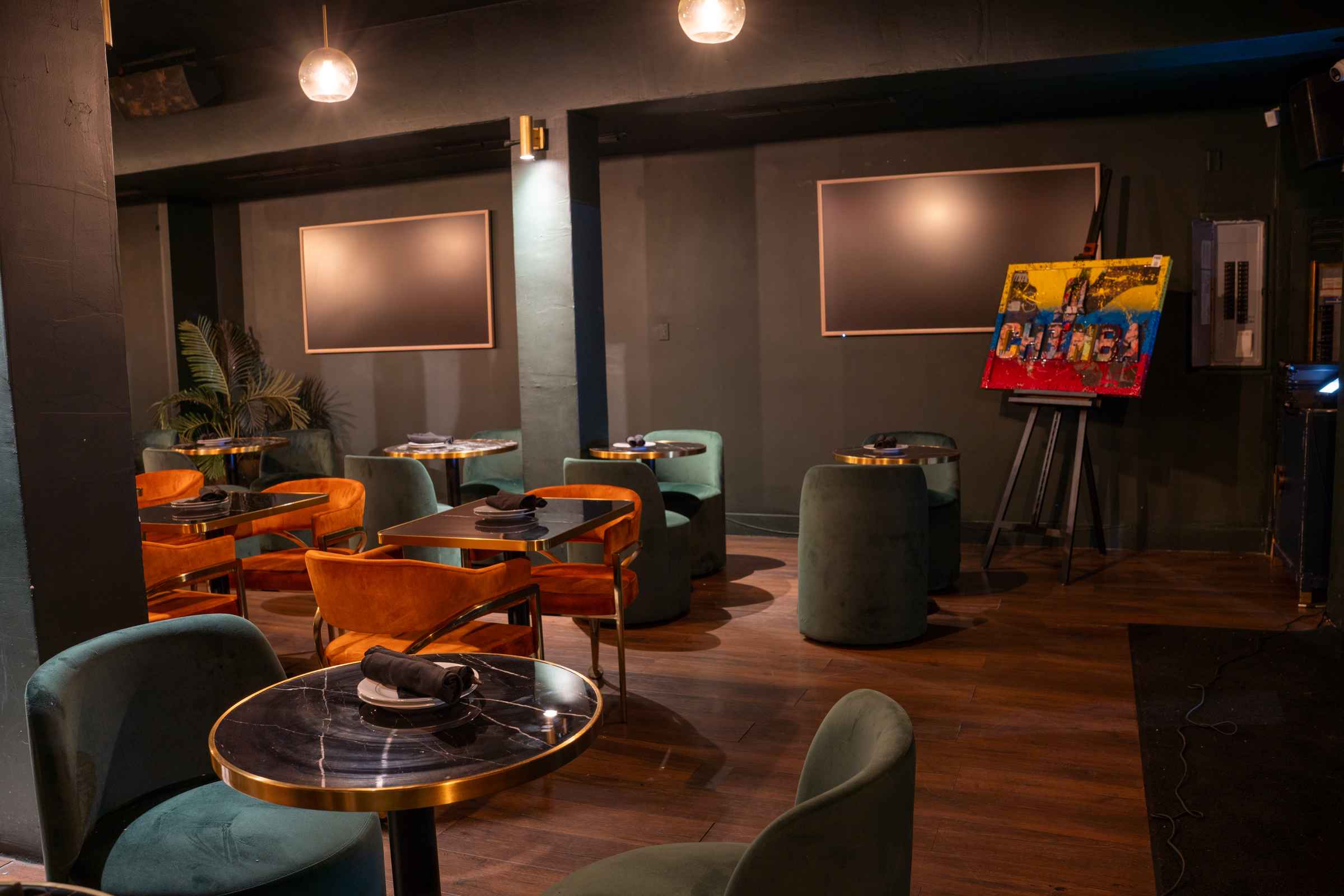 Lounge seating area with rust orange and green velvet chairs and round brass-trimmed tables inside Spanglish Martini Bar in Wynwood, Miami